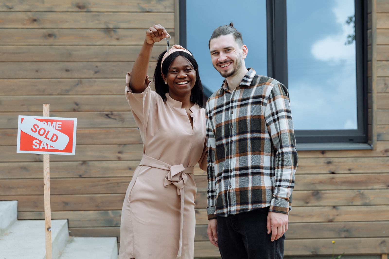 Couple holding the keys outside their first home, next to a sold sign